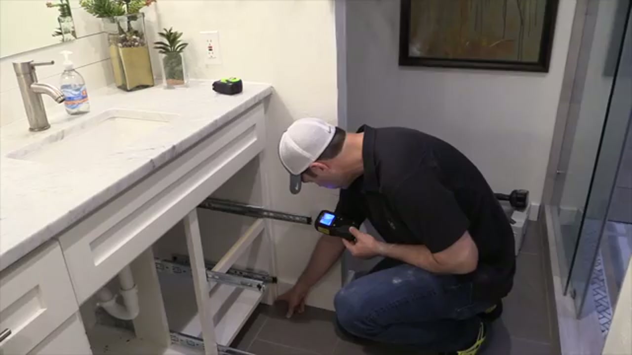 Technician using a thermal imaging camera to scan an interior wall for hidden water leaks.